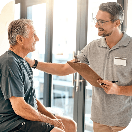 An older man has a friendly conversation with a person holding a clipboard.