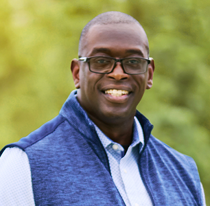 Head shot of Rorey, a smiling man wearing glasses and a blue vest who lives with CIDP